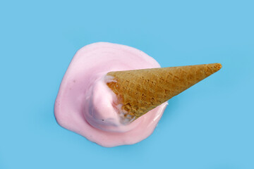 Melting ice cream ball with waffle cone on blue background.