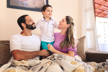 Parents and child embracing on the couch, sharing affectionate gestures. Their smiles and warmth create a joyful, heartfelt scene. Ideal for showcasing authentic, loving family interactions at home