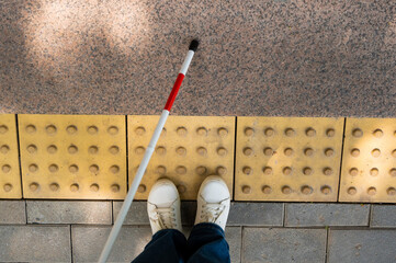 Close-up of female foot, walking stick and tactile tiles.