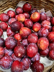 Red plum fruits from freezer or fridge with cold skin on top fruit bamboo ratan basket storage isolated on vertical ratio background.