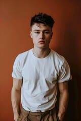 Obraz premium Un guapo hombre joven posando, vistiendo una playera blanca mockup al fondo una pared en tonos naranja. Moda casual