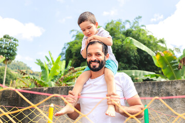 Dad carries his young son on his back, both smiling and enjoying playful moments. The image radiates love, affection, and celebrates fatherhood. 