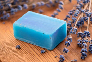 A bar of handmade soap rests on a wooden table, elegantly adorned with delicate lavander flowers.