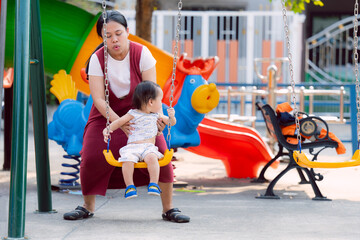 Mother is taking her son to ride the yellow swing at the playground, excitement and fun with...