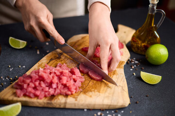 Woman cut tuna steak into slices on a wooden cutting board at domestic kitchen