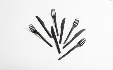 A set of plastic disposable tableware, including forks and knives, arranged in a row on a white background. Recycling concept.