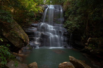 Obraz premium A medium-sized waterfall among rocks and bushes, with a water source and submerged rocks