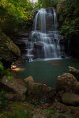 Obraz premium A medium-sized waterfall among rocks and bushes, with a water source and submerged rocks