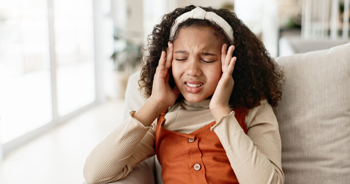 Young girl, headache and sofa with stress in anxiety, pain or distress for noise at home. Little female person, child or kid alone with migraine on living room or lounge couch in fatigue or burnout