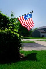 An American flag waves against a backdrop of greenery and a clear blue sky, symbolizing patriotism.