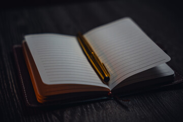 A notebook with a gold pen on the table in the candlelight