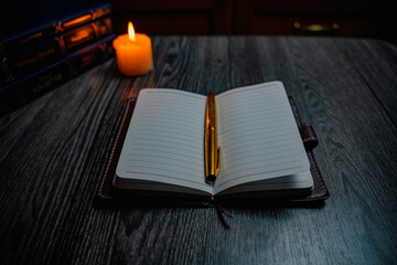 A notebook with a gold pen on the table in the candlelight