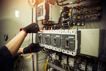 Electricity and electrical safety maintenance service system, Technician hand checking electric current voltage at circuit breaker terminal and cable wiring in main power distribution board.