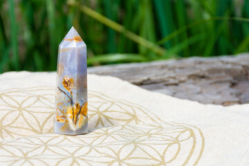 An image of a flower agate crystal healing tower and sacred geometry grid cloth on a driftwood log. 