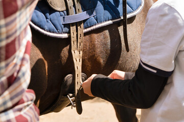 People adjusting saddle straps on horse.