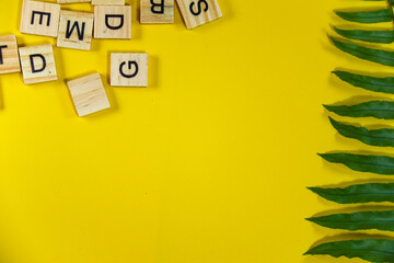 Beautiful bright summer yellow background with  green tropical plant branch and wooden alphabet...