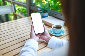 Mockup image of a woman holding mobile phone with blank desktop screen in cafe