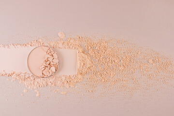 A block of compact powder in a natural tone with the texture of broken pieces stands on a swatch of...