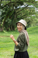 A joyful young girl wearing a green hat and sweater smiles brightly while standing in a lush green field.