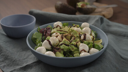 Man making salad with mixed greens avocado and mozzarella in blue bowl
