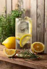 Summer refreshing drink with ice, rosemary and lemon slices on a old wooden table.