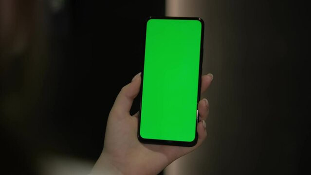 In the image, a woman is seen holding a cell phone with a green screen display