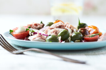 Salad with tuna, green olives and cherry tomatoes. Bright wooden background. Close up. Copy space.