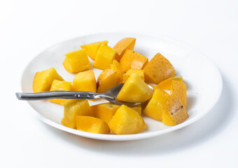Ripe delicious sliced mangoes on white background served ready to eat with spoon on white plate.