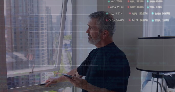Middle-aged Caucasian man holding smartphone and looking out a window