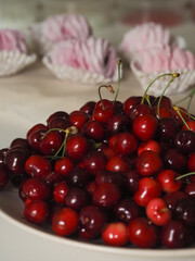 Vertical close up shot of a heap of fresh cherries in a plate and a tray with homemade pink zefir in the backdrop. Healthy and delicious treats during the master class. .
