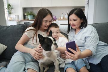 Asian family mother with children sitting at home on sofa in apartment while spending time with pet dog