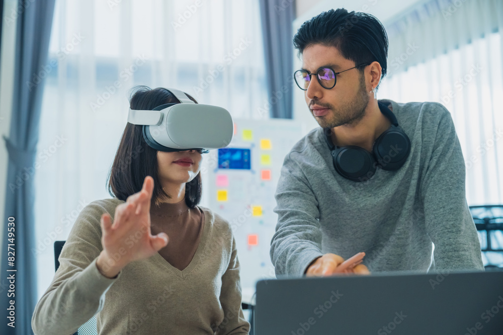 Wall mural asian software developer wearing a virtual reality headset works on a vr project, with a colleague f