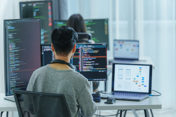 Asian software developers working on multiple screens displaying code and application diagrams in a...