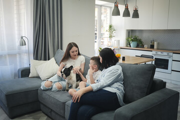 Asian family mother with children sitting at home on sofa in apartment while spending time with pet dog