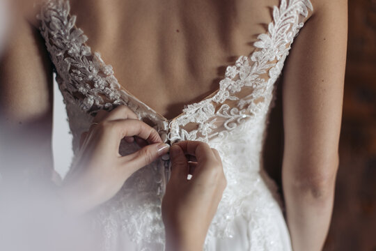 Bridemaid's hands fastening a detailed lace wedding dress