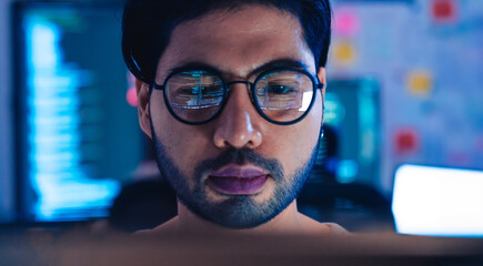 Close-up of a programmer intensely focused on his work, with computer code reflecting in his...