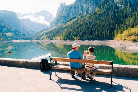 dad and son eat ice cream in summer near a mountain lake