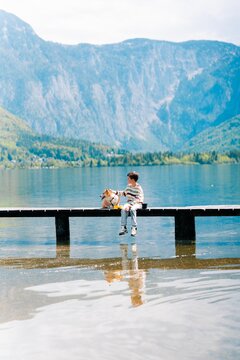 boy on lake near Alps in mountain Austria with corgi dog, best friends