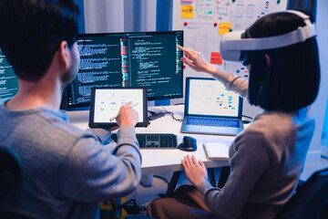 Asian software developer wearing a virtual reality headset works on a VR project, with a colleague...