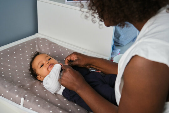 African mother is dressing up her baby girl on a changing table.