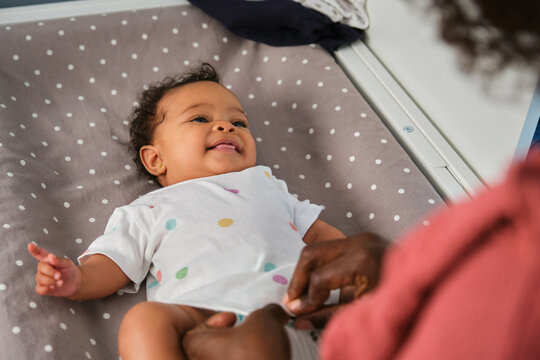 A smiling baby is being dressed up by her mom on a changing table.