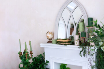 Fireplace with a mirror above it. Interior design living room with a white fireplace and carved mirror. Fireplace decorated with candles, stabilization moss, decor, globe, green plants and books. 