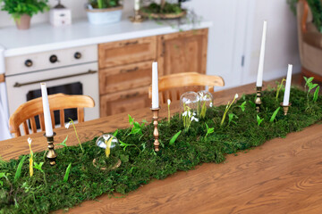 Interior of table for guests with natural decor and candles. Festive decorated eco Composition on table with of natural green stabilization moss, plants and snowdrops flowers under flask dome.	
