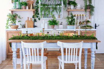 Cozy Wooden cuisine cabinet furniture, utensil, decorations and houseplants on shelves. Dining room with table and chairs. Stylish Interior home kitchen in scandinavian style with green plants in pots