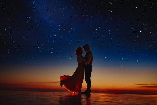 Silhouette of a couple dancing on the beach at twilight with a stunning starlit sky and the glow of sunset in the background - Powered by Adobe