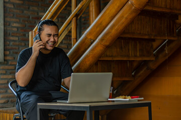 Young Asian man, digital nomad working remotely from cafe, using laptop and smartphone. young Asian men are hanging out in a cafe with an industrial theme