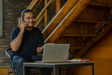 Young Asian man, digital nomad working remotely from cafe, using laptop and smartphone. young Asian men are hanging out in a cafe with an industrial theme