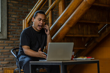 Young Asian man, digital nomad working remotely from cafe, using laptop and smartphone. young Asian men are hanging out in a cafe with an industrial theme