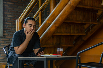 Young asian men, digital nomad working remotely from a cafe, using  smartphone.