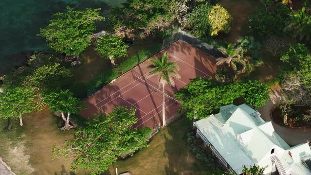 Aerial view of a tennis court surrounded by lush greenery and tropical trees in Jamaica. Serene environment with a building nearby